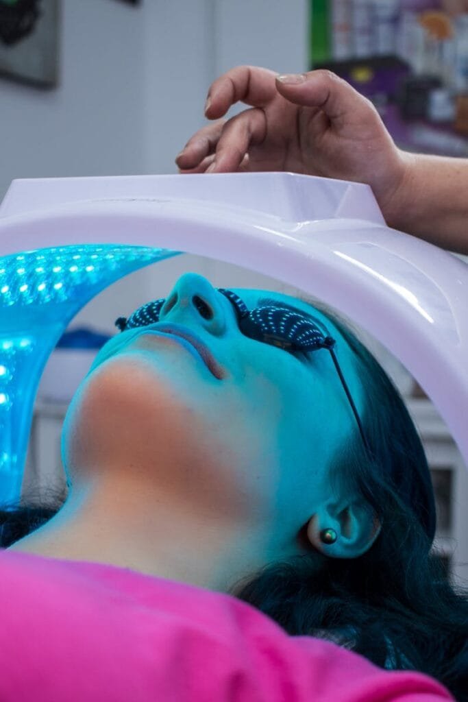 Unrecognizable woman with dark hair with pierced ears lying under ultraviolet lamp while visiting contemporary clinic and spending time in modern salon
